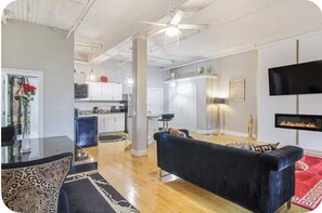 A modern living room with a black sofa, a dining area with a glass table, and a kitchen in the background.