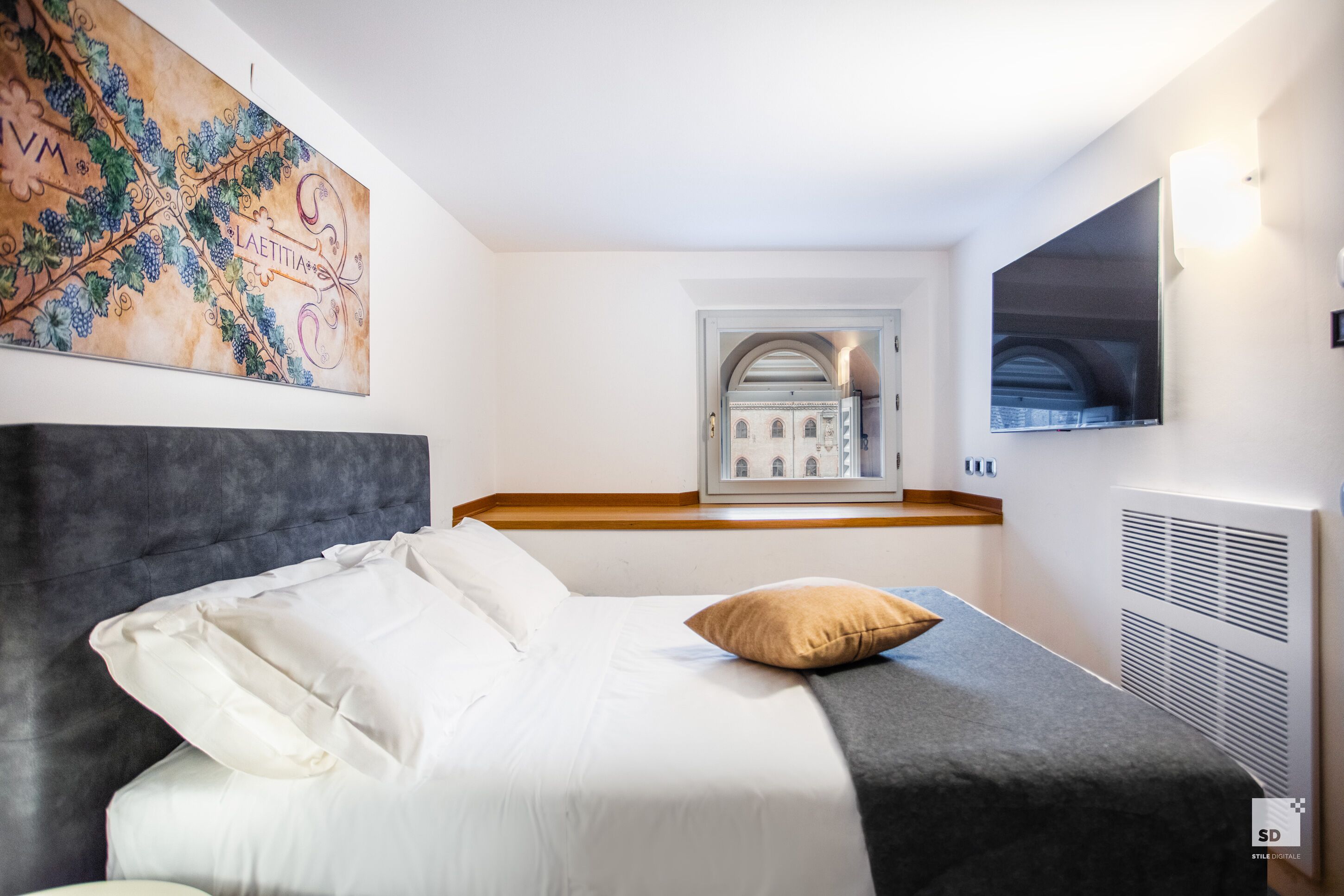Ein modernes Hotelzimmer mit einem Bett, einem großen Kunstwerk an der Wand, einem Fernseher und einem Fenster mit Blick auf ein Gebäude.