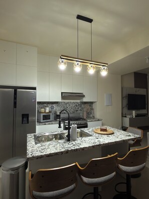 A modern kitchen with a granite countertop, stainless steel appliances, a central island with bar stools, and pendant lighting. - Villa privada con jacuzzi, piscina; en el corazón de Punta Cana (Punta Cana)