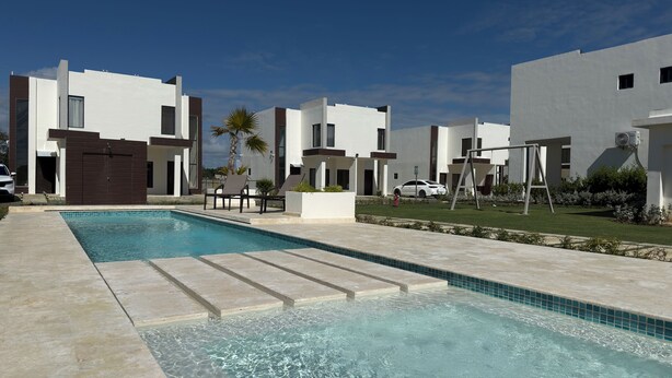A swimming pool with lounge chairs, a white car, and modern buildings in the background. - Relax, Unwind & Enjoy Punta Cana at The Grace Place (Punta Cana)