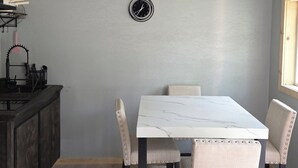 Un comedor con una mesa de mármol blanco y cuatro sillas tapizadas. Un reloj está colgado en la pared sobre la mesa.