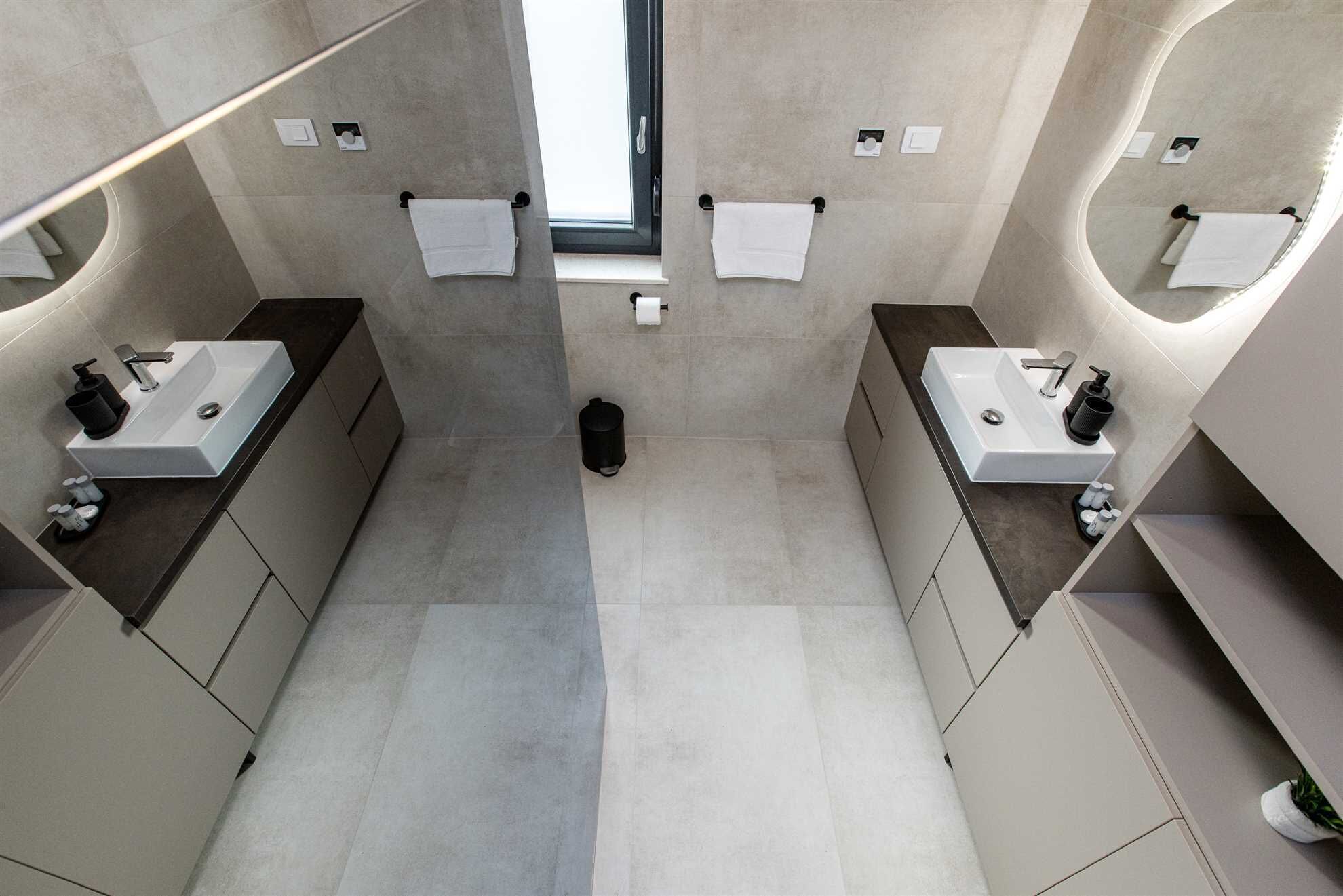 A modern bathroom with two sinks, a toilet, and a trash bin.