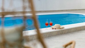 A poolside area with a clear view of the water, two glasses of red beverage, and a straw.