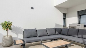 A modern outdoor seating area with a grey sectional sofa, a wooden coffee table, and a potted plant.