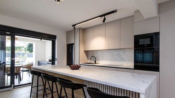 A modern kitchen with a marble countertop, black bar stools, and a Bosch oven.