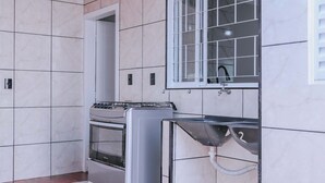 Una cocina con horno empotrado, un lavamanos con manguera y una ventana con persianas.