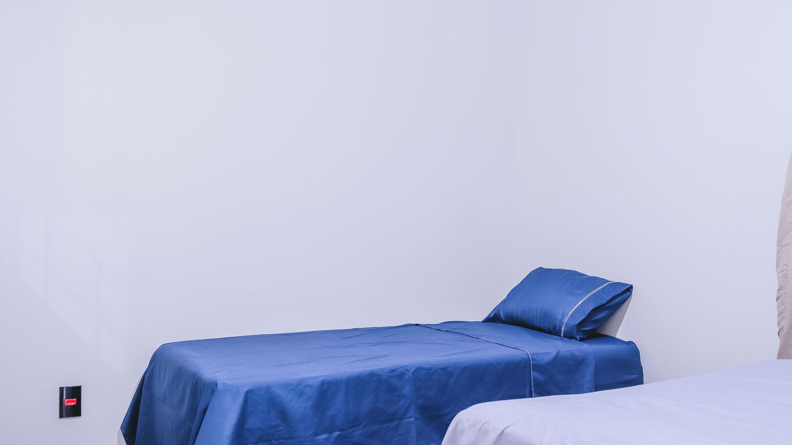 Ein kleines Zimmer mit einem Einzelbett, einer blauen Bettdecke und passenden Kissen.