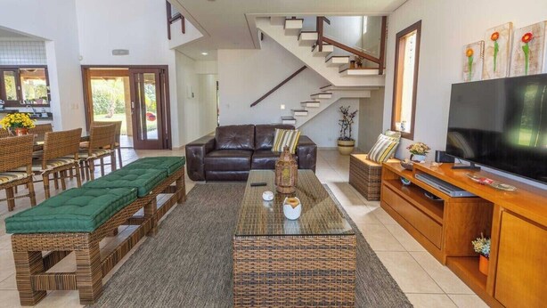 Una sala de estar amplia con sofá, mesa de centro y mueble para la televisión. Se ve una escalera que sube a un nivel superior.