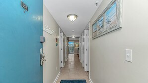 Un pasillo de hotel con una puerta azul marcada con el número 555, un teclado de seguridad, un felpudo y un cuadro en la pared.