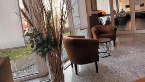 Et moderne interiør med en siddeplads bestående af to brune lænestole og en høj, dekorativ plante nær et stort vindue.