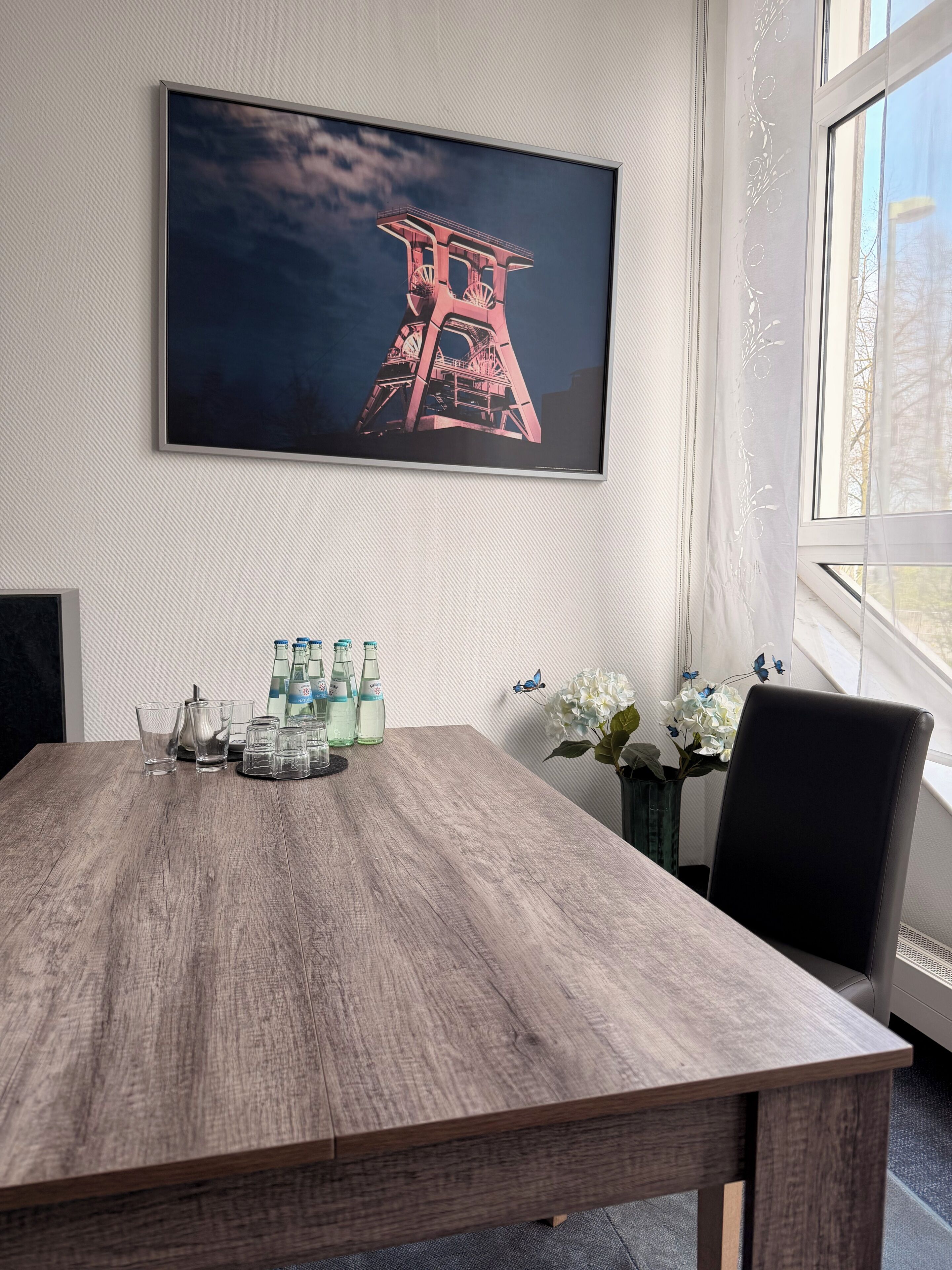 A conference room with a wooden table, a framed picture of a tower, and a window with a view.