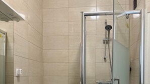 Un baño moderno con ducha envuelta en vidrio, un lavabo blanco y una lavadora pequeña.