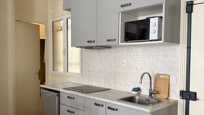 Una cocina compacta con armarios grises, microondas integrado, un lavamanos y lavavajillas.