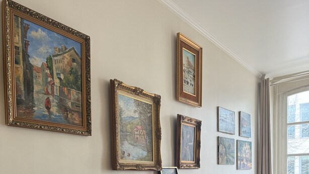 Un piano de cola en una habitación con piso de madera, un banco y varias pinturas enmarcadas en la pared.