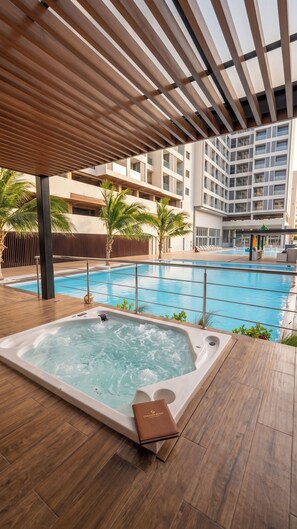 A swimming pool with a hot tub, wooden deck, and a modern building in the background.