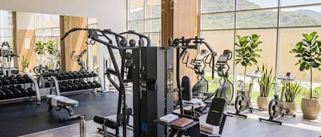 A gym with various exercise equipment, large windows, and a view of the outdoors.