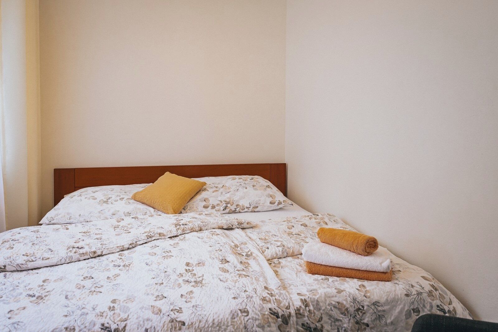 A neatly made bed with floral bedding, a wooden headboard, and a single yellow pillow.