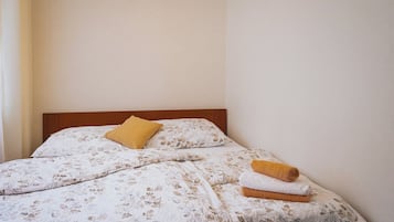 A neatly made bed with floral bedding, a wooden headboard, and a single yellow pillow.