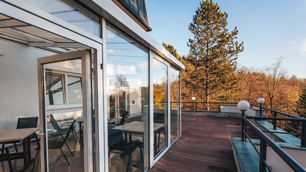 A modern outdoor deck with glass doors, wooden flooring, and outdoor furniture. - Penzion U Libuše (Luleč)