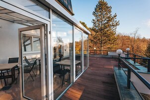 A modern outdoor deck with glass doors, wooden flooring, and outdoor furniture.