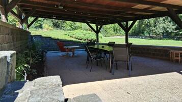 An outdoor patio with a table and chairs, a stone wall, and a view of a grassy area with trees.