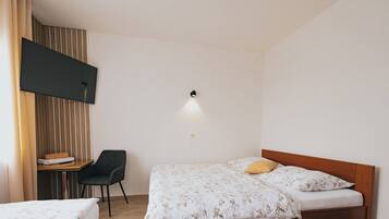 Une chambre avec deux lits, un bureau, une chaise et un téléviseur fixé au mur.