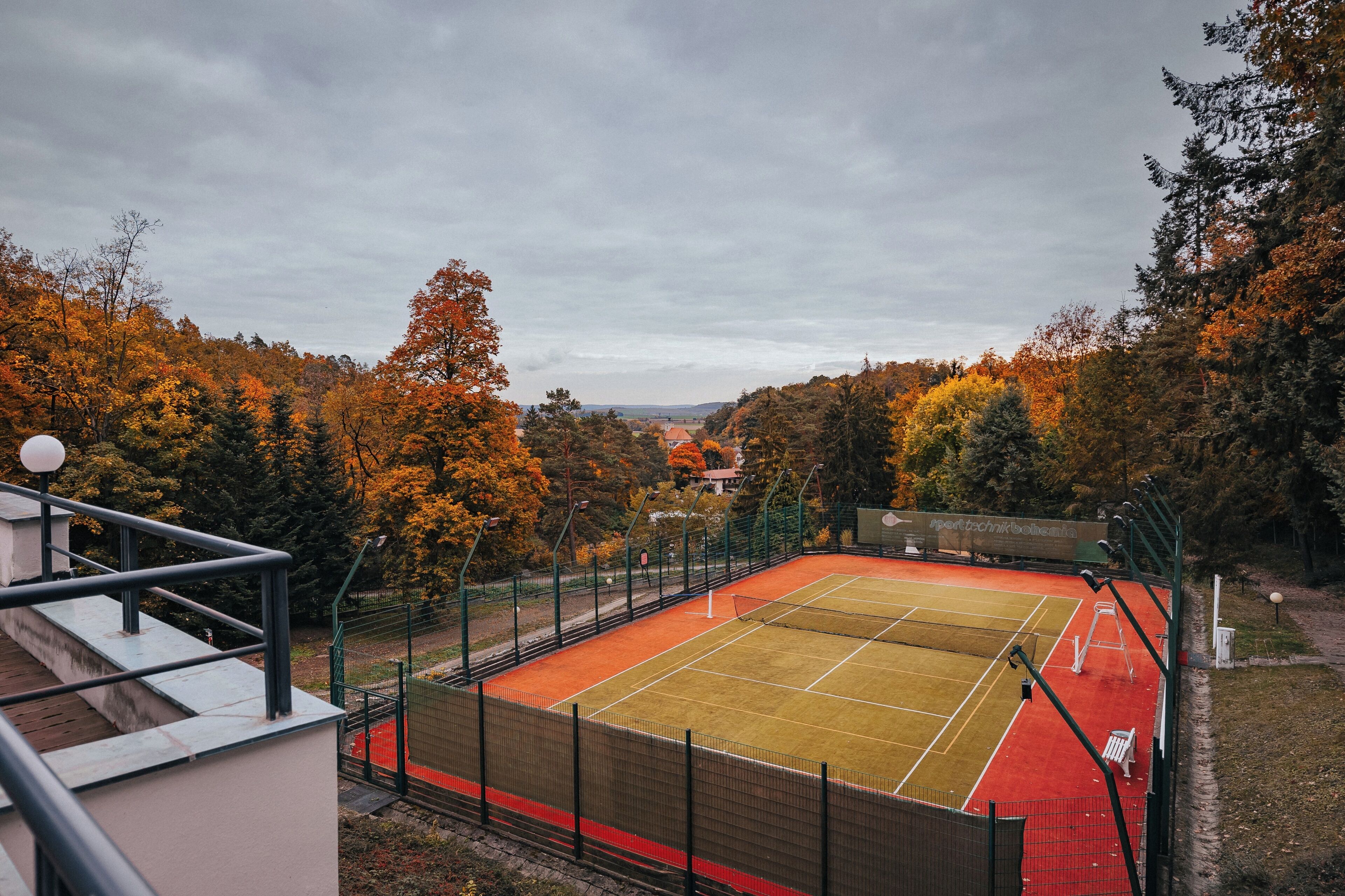 An outdoor tennis court surrounded by trees with autumn foliage.