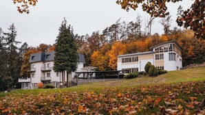 A multi-story building with balconies, a covered outdoor area, and a surrounding landscape with trees and fallen leaves. - Penzion U Libuše (Luleč)