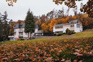 A multi-story building with balconies, a covered outdoor area, and a surrounding landscape with trees and fallen leaves.