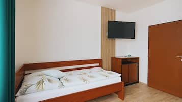 A single bed with a wooden frame, a small bedside table, a television mounted on the wall, and a wardrobe.