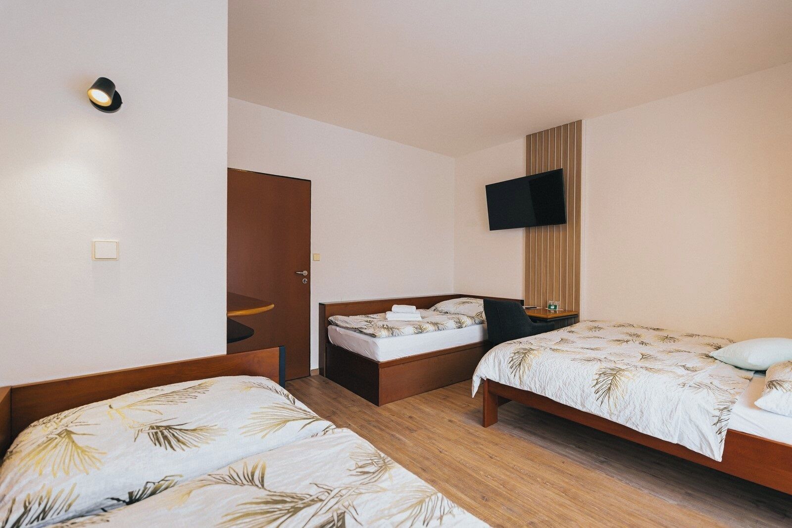 Habitación de hotel con dos camas individuales, un televisor montado en la pared y piso de madera.