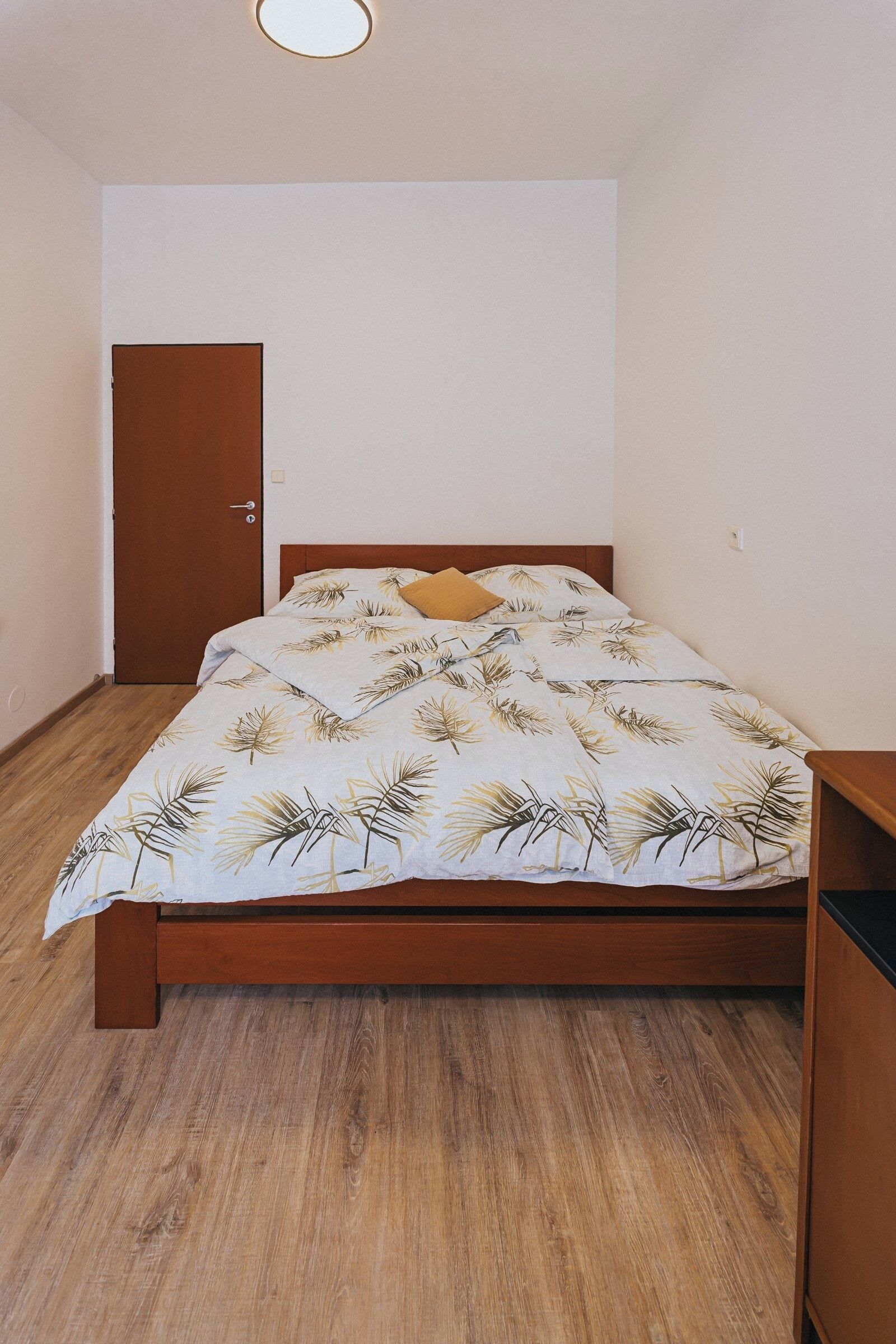 Une chambre à coucher avec un lit, un plancher en bois, une porte et un luminaire fixé au mur.