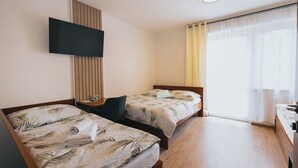 A hotel room with two beds, a TV mounted on the wall, a desk, and a window with curtains. - Penzion U Libuše (Luleč)