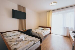 A hotel room with two beds, a TV mounted on the wall, a desk, and a window with curtains.