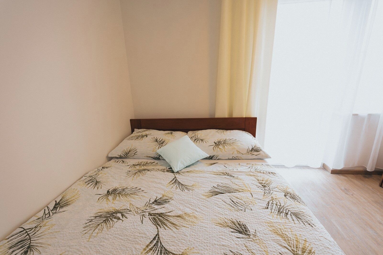 A neatly made bed with a leaf-patterned bedspread, a wooden headboard, and a light blue pillow.