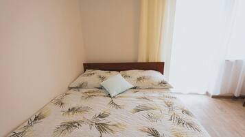 A neatly made bed with a leaf-patterned bedspread, a wooden headboard, and a light blue pillow.