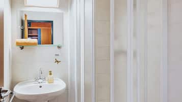 A bathroom with a white sink, a glass shower enclosure, a mirror, and a red rug.