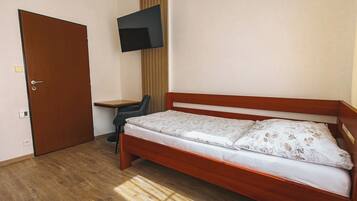 A room with a wooden bed, a desk, a chair, a TV mounted on the wall, and a door.