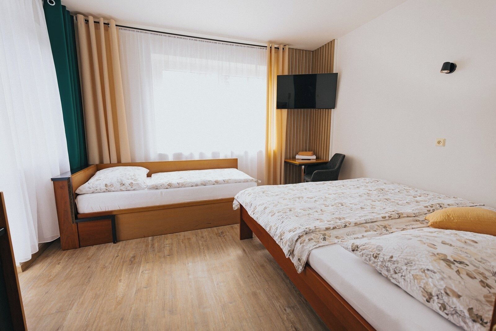 A hotel room with two beds, a desk, a chair, a TV, and a window with curtains.
