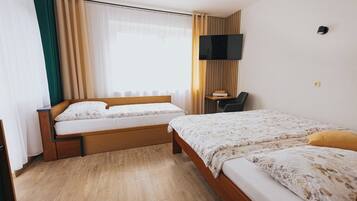 A hotel room with two beds, a desk, a chair, a TV, and a window with curtains.
