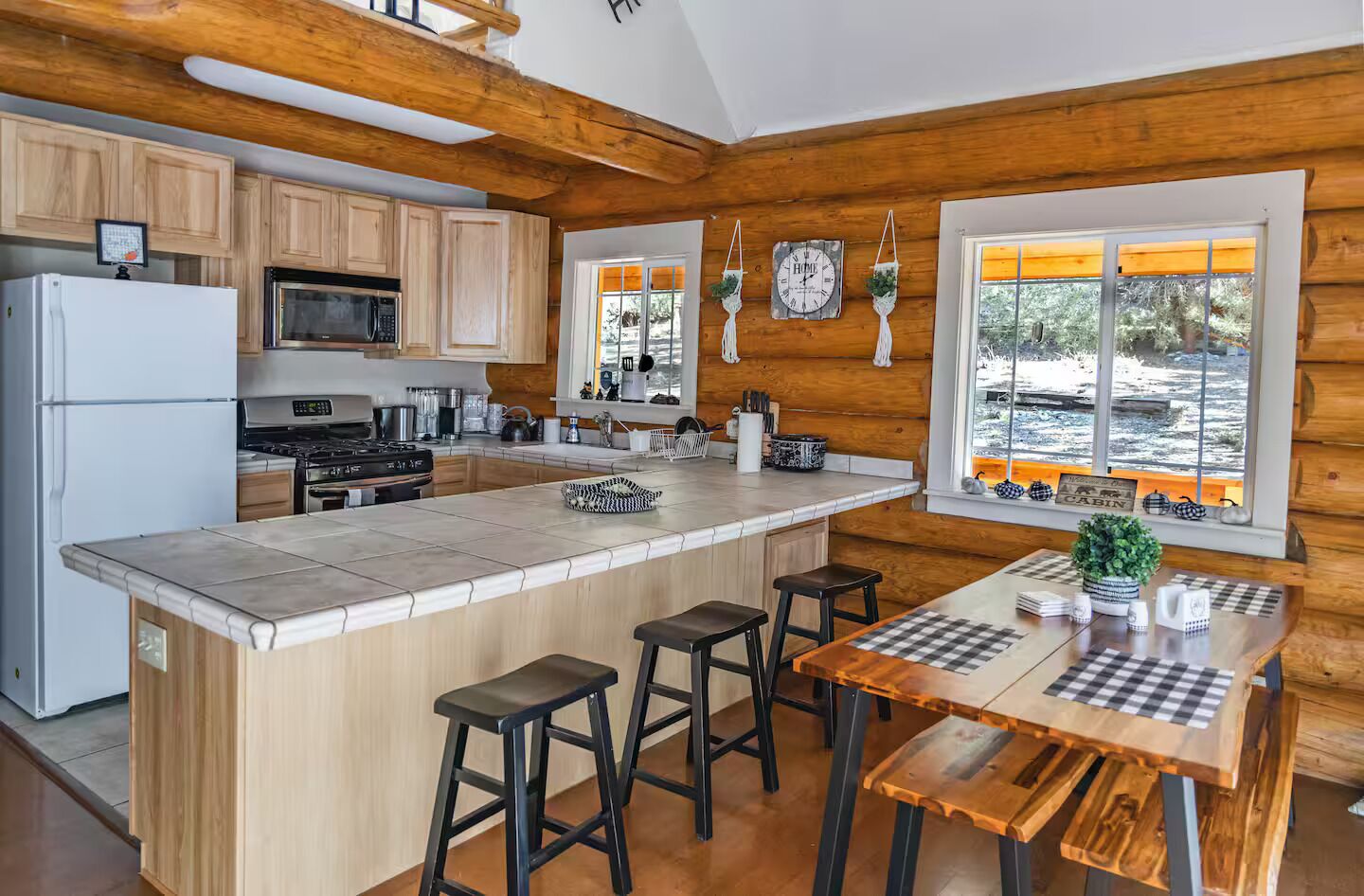 Una cocina moderna con armarios de madera, una isla central con taburetes y vistas al exterior a través de amplios ventanales.