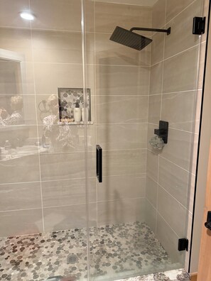 A modern shower with a glass door, a rain showerhead, and a tiled floor with a circular pattern.