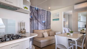 Una cocina moderna con estufa integrada, un área de comedor con mesa y sillas, un sofá con cojines a rayas y una pared decorativa con diseño geométrico.