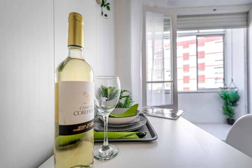 Uma garrafa de vinho branco e um copo sobre uma mesa, com vista para a janela.
