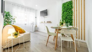 Un salon moderne comprenant un canapé, une table à manger avec des chaises, un téléviseur fixé au mur et un jardin vertical verdoyant.