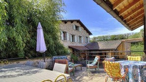 Un patio al aire libre con una mesa y sillas, una zona de estar cubierta y un edificio de piedra al fondo.