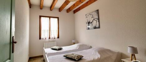Un dormitorio con dos camas, una ventana, un radiador y un cuadro en la pared.