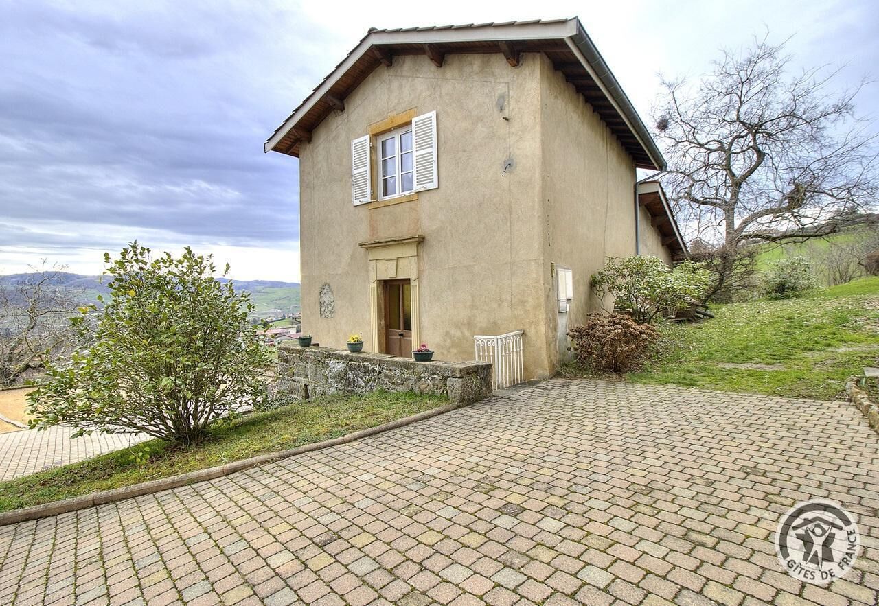 A two-story house with a stone facade, a small porch, and a view of the countryside.