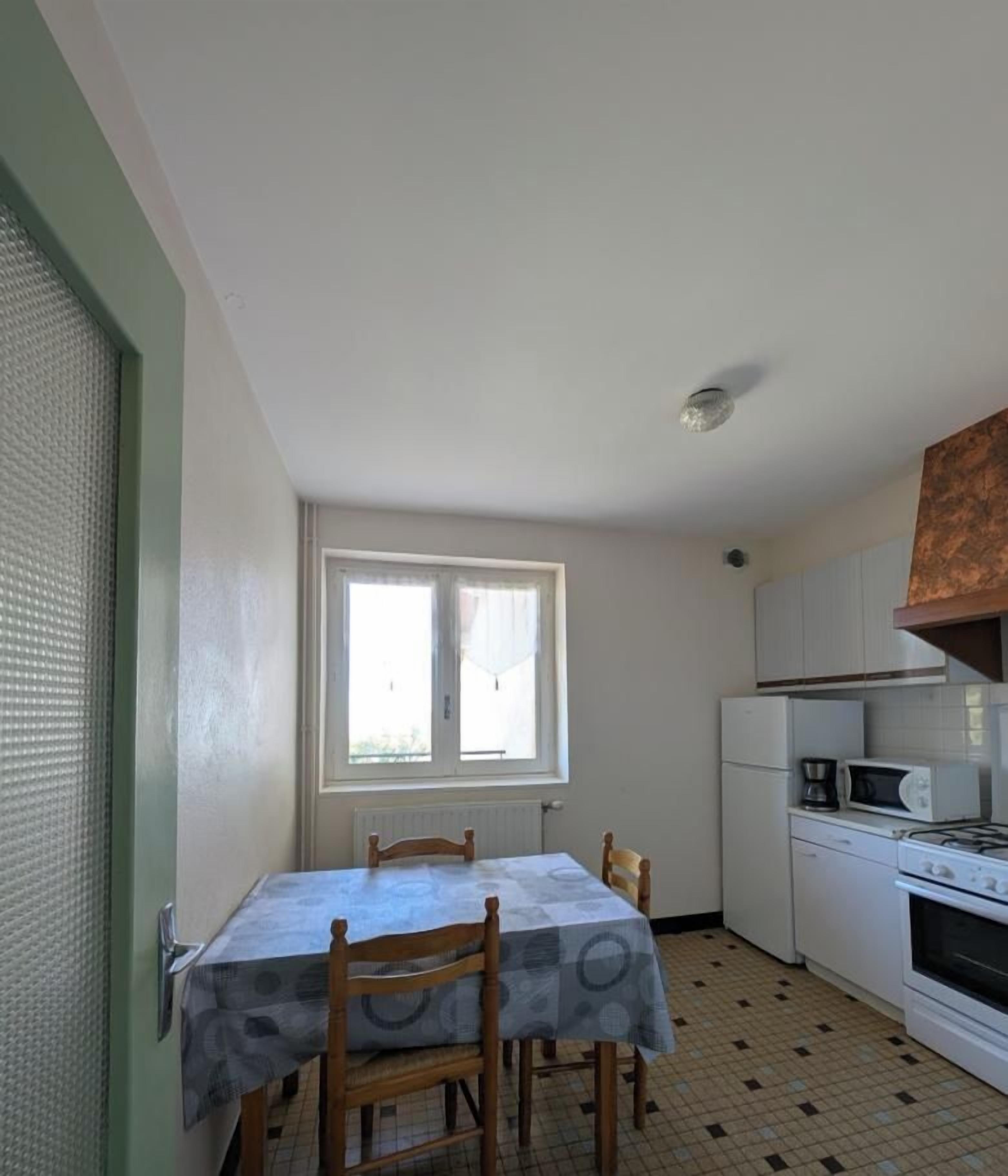 Een kleine keuken met een eettafel, stoelen, een raam en basisapparatuur.