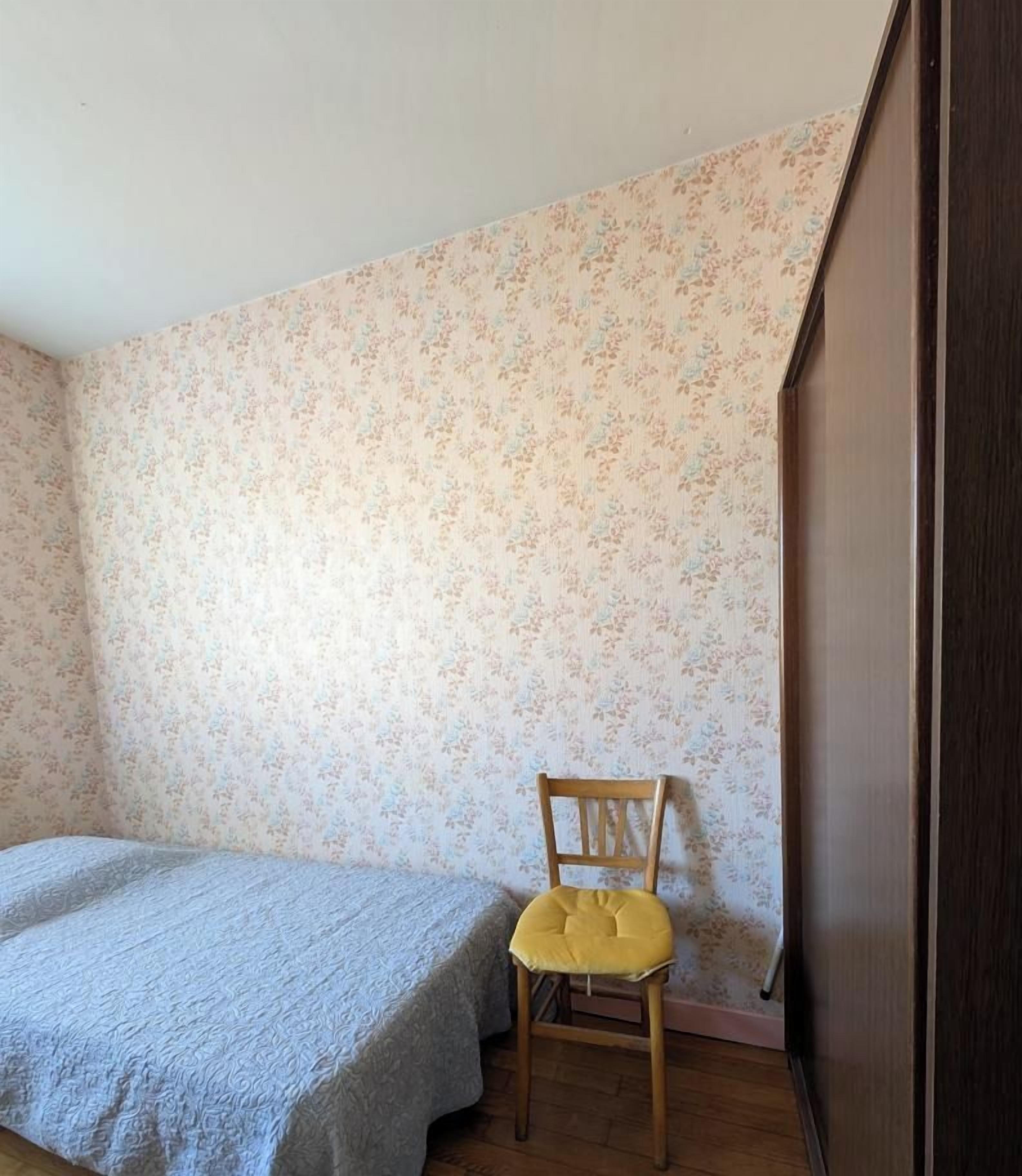 Une petite pièce avec un lit simple, une chaise en bois et une armoire.